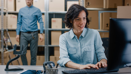 Female Inventory Manager Sitting at Her Desk and Using Personal Computer, Worker Puts Packages on...