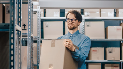 Warehouse Worker Holds Cardboard Box. In the Background, Rows of Shelves Full of Cardboard Boxes...