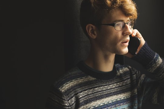 Young Man Wearing Eyeglasses Talking On Cell Phone At Home