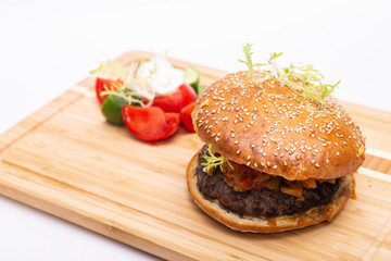 Fast food. Tasty burger with  tomato and cucumber salad on a wooden board.
