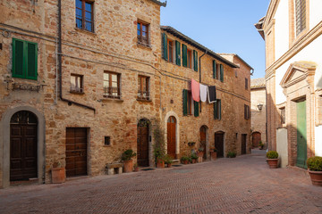 Old street of medieval town Pienza are decorated with flowers in the flowerpots, Italy