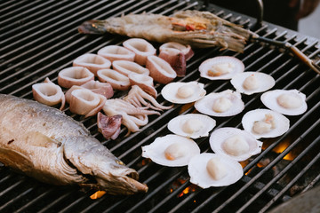 delicious prawn, fish, shell and squid spit on grill with flames in background