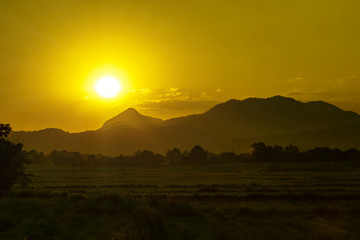 Naklejka na ściany i meble Sunset over silhouette mountain and rice field in evening