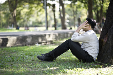 Business man failing and serious under tree in the park. He is stressed with work Unsuccessful disappointed in project