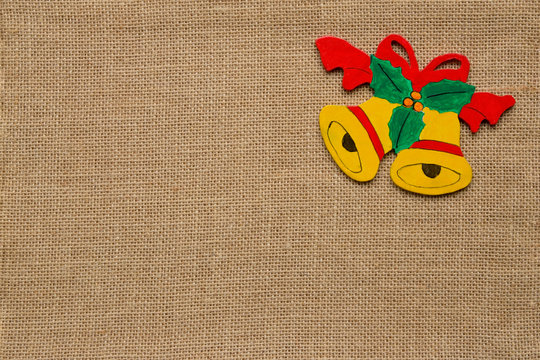 2 gelbe Glocken mit roter Schleife und Stechpalme Ornament aus Holz mit grossem Textfeld auf Hintergrund aus Jute