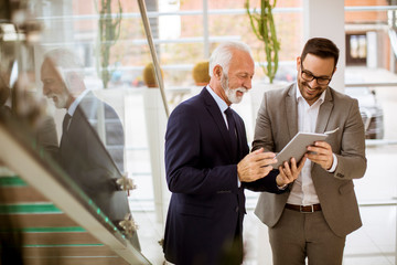 Senior businessman pointing and showing something to junior partner on digital  tablet at office