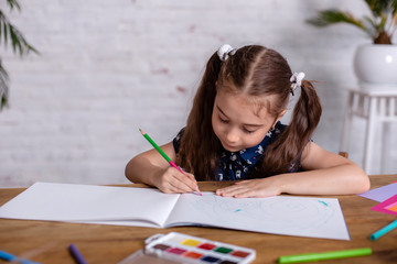 Inspired little girl at the table draw with crayons or do home work