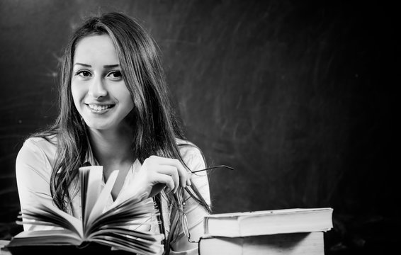 young smiling teacher portrait with open books at classboard desk