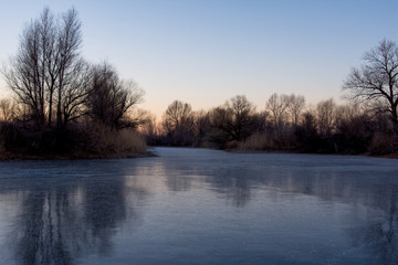 Beautiful landscape of forest lake in the early morning. Frozen lake in the forest. The reflection on the ice.
