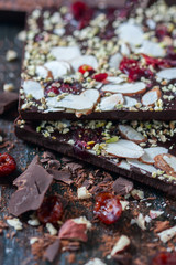 Homemade dark chocolate bar with dried berries and nuts on black background