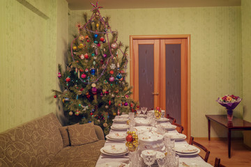 Served table with festive tableware near beautiful decorated Christmas tree in living room interior. Concept of new year holiday at cozy home. Vintage tone
