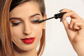 Woman applying mascara on her eyelashes against white background