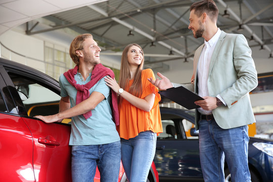 Salesman with clipboard consulting young couple in modern car dealership