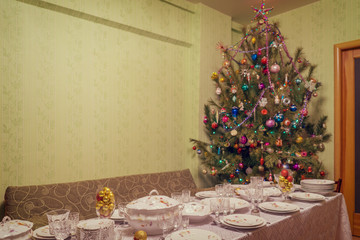 Served table with festive tableware near beautiful decorated Christmas tree in living room interior. Concept of new year holiday at cozy home. Selective focus, vintage tone