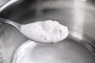 Chemical reaction of vinegar and baking soda in spoon over saucepan, closeup