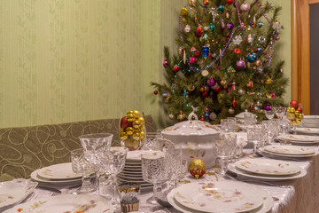 Served table with festive tableware near beautiful decorated Christmas tree in living room interior. Concept of new year holiday at cozy home