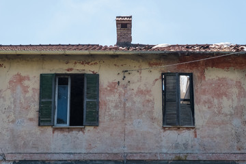 Green wooden windows and chimney on the roof of an old worn house.