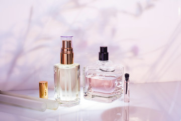 Different perfume bottles and sampler on a pink floral background. Selective focus. Perfumery...