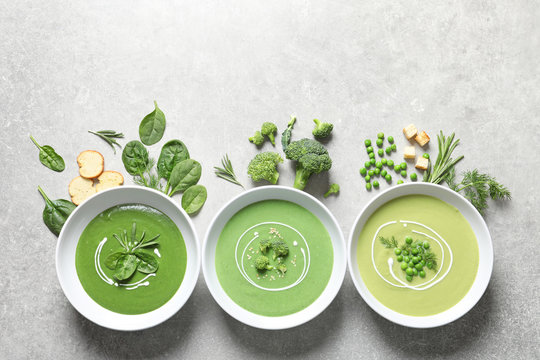 Dishes with different fresh vegetable detox soups made of green peas, broccoli, spinach and ingredients on table, flat lay