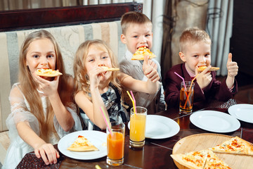 Les enfants mangent des pizzas au restaurant.