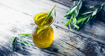 Fresh olive oil in carafe with olive twig on wooden table.