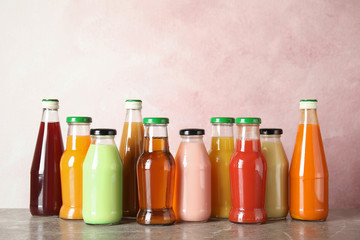 Bottles with different drinks on table against color background