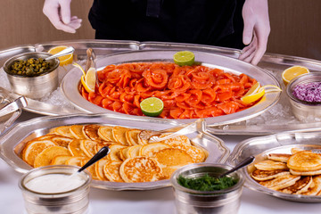 Red fish with a lime and a lemon, is served with pancakes, sour cream and greens