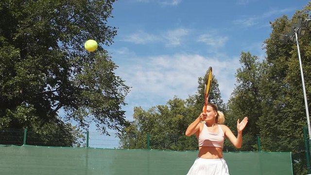 Cheerful woman in tennis outfit exercising in serving outdoor, summer morning starts with tennis training