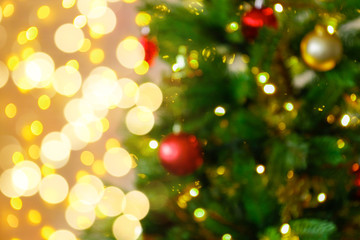 Fototapeta na wymiar Decorated Christmas tree on soft yellow lights with bokeh effect background. Festive composition with fir and blurry sparkling backdrop, new year holiday decorations. Close up, copy space.