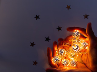 Hands with light bulbs in shape of heart. Metal light bulbs with delicate pattern shine in dark. Holiday decoration with magic light reflections.