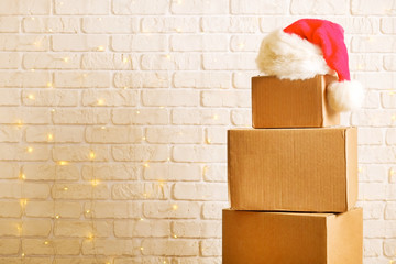 Blank brown freight box with Santa Claus hat on top, brick wall with Christmas lights on background. Moving company / delivery service holiday deals promotion concept. Copy space, close up.