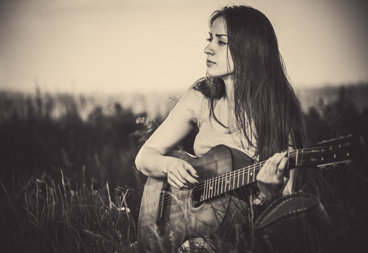 pretty woman playing old guitar in high meadow grass