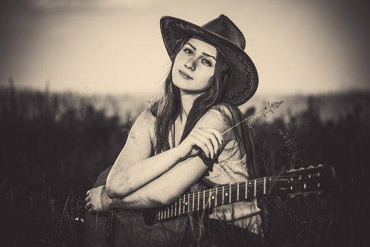 young nostalgic woman with old guitar at meadow grass