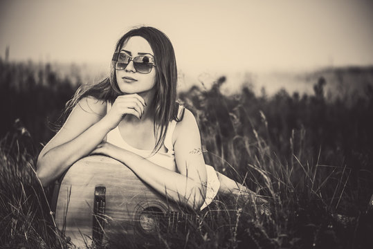 young woman in sunglasses with old guitar at meadow grass