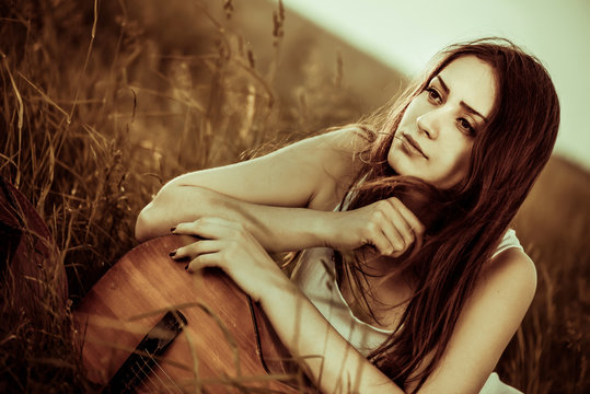 young pretty woman with old guitar portrait at rural meadow grass