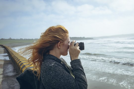 Side view of woman taking picture with camera on beach