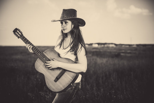 young woman in hat playing guitar at rural meadow background