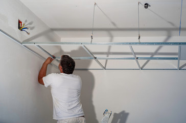 Construction worker assemble a suspended ceiling with drywall and fixing the drywall to the ceiling metal frame with screwdriver.