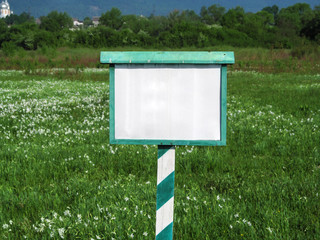 Blank white and green signage close-up against the background of a blooming valley in summer. Simple minimalist template with copy space, nature conservation concept