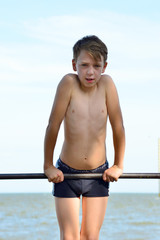 A boy in shorts goes in for sports on a horizontal bar on the street. Does various exercises, pull-ups, pushups and hangs upside down. © andov