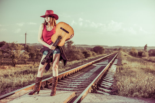 lovely brunet in hat with guitar at rural railways