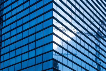 Construction crane reflected in modern glass facade, construction industry concept.