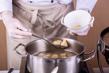 The cook gets a spoon boiled pelmeni from the boiling pan