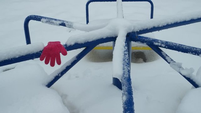 Forgotten children glove lies on bench of the rotating carousel in the winter snow day 