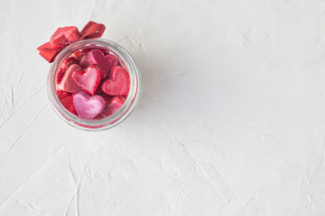 Fototapeta na wymiar Valentine's day concept. jar with small hearts red and pink on a light background.