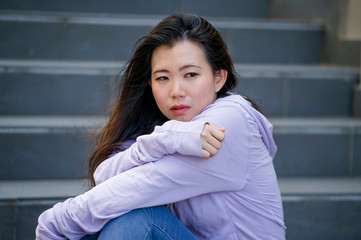 depressed Asian American student woman or bullied teenager sitting outdoors on street staircase...