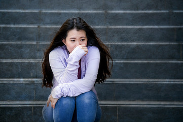depressed Asian Chinese student woman or bullied teenager sitting outdoors on street staircase...