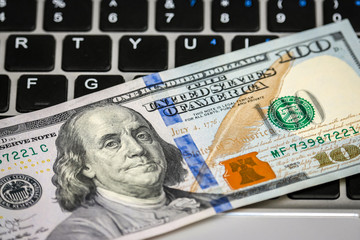 Closeup view of one hundred dollar banknote lying on the laptop keyboard.