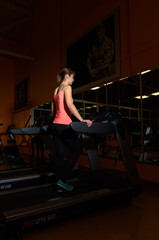 Fototapeta na wymiar A young woman runs on a treadmill in a sports club, is engaged in a fitness sports club