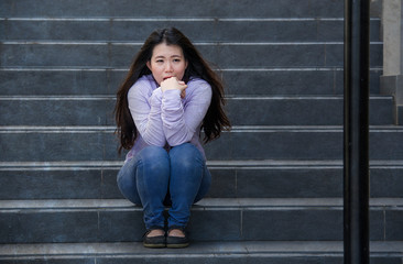 depressed Asian Japanese student woman or bullied teenager sitting outdoors on street staircase...